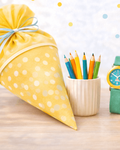 Schultuete gefüllt, daneben Stifte und Armbanduhr für Kind als Schulstart Geschenk